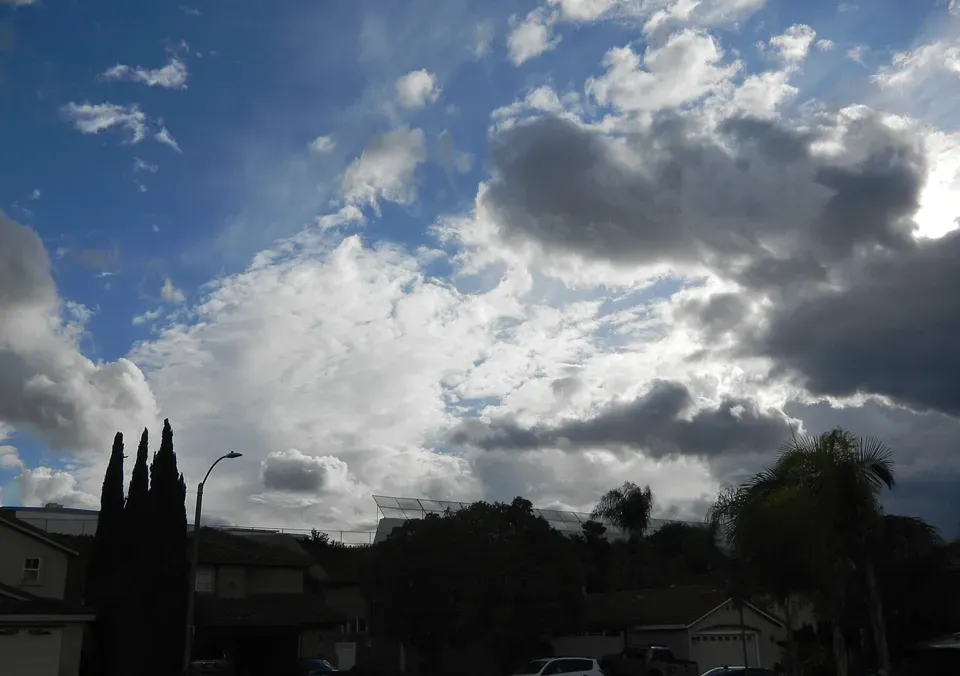 Dunkle Regenwolken über Häusern und Palmen.